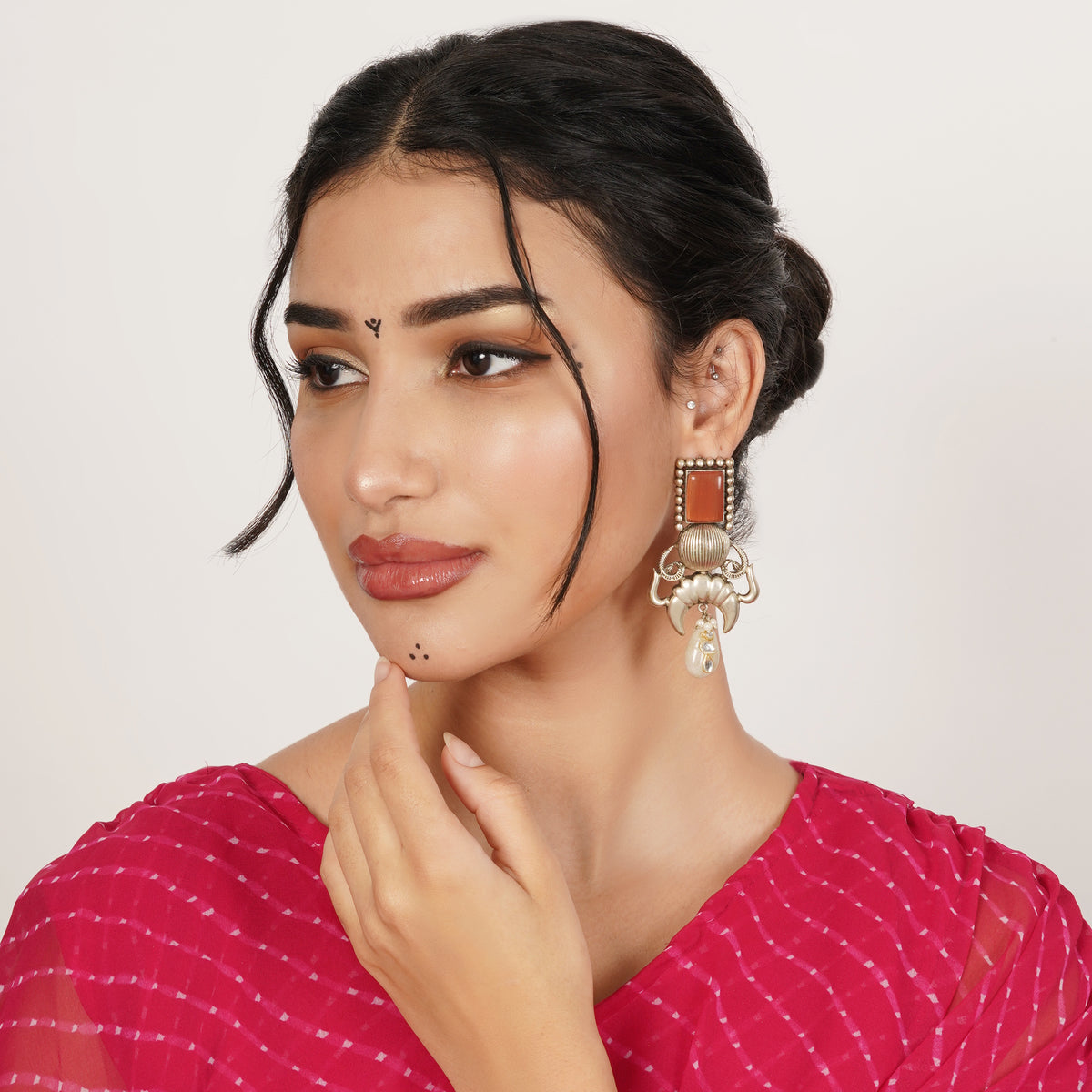 A large gold-toned statement earring with a rectangular orange stone and pearl drop