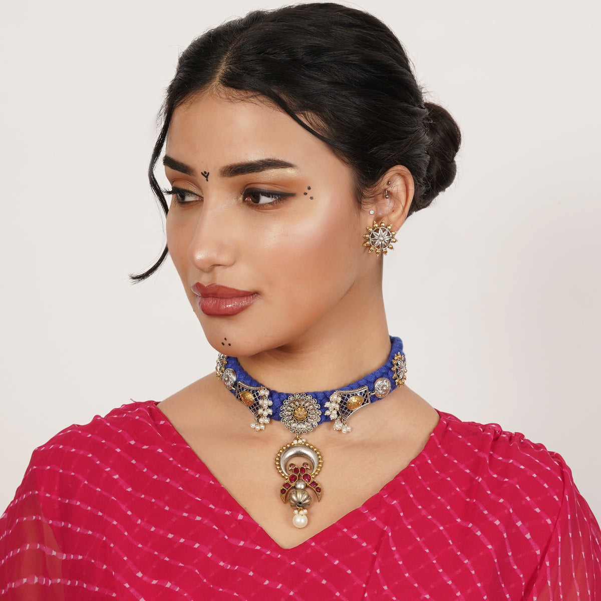 A woman wearing a blue beaded choker necklace with gold and silver-toned embellishments and a matching ornate pendant