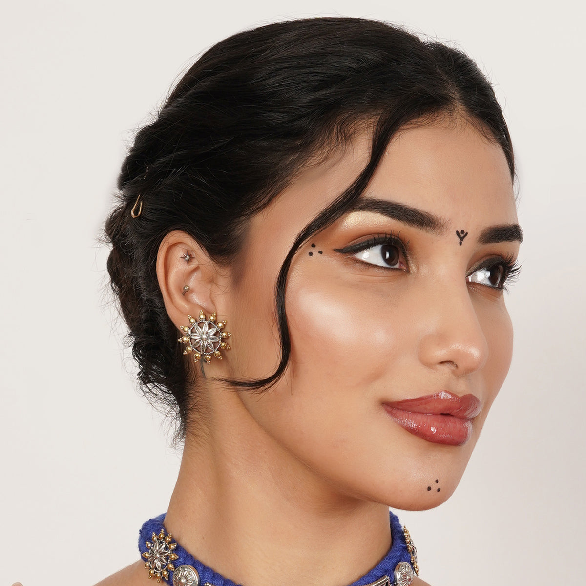 A close-up wearing a gold-toned starburst stud earring with clear stones, a blue embellished choker.