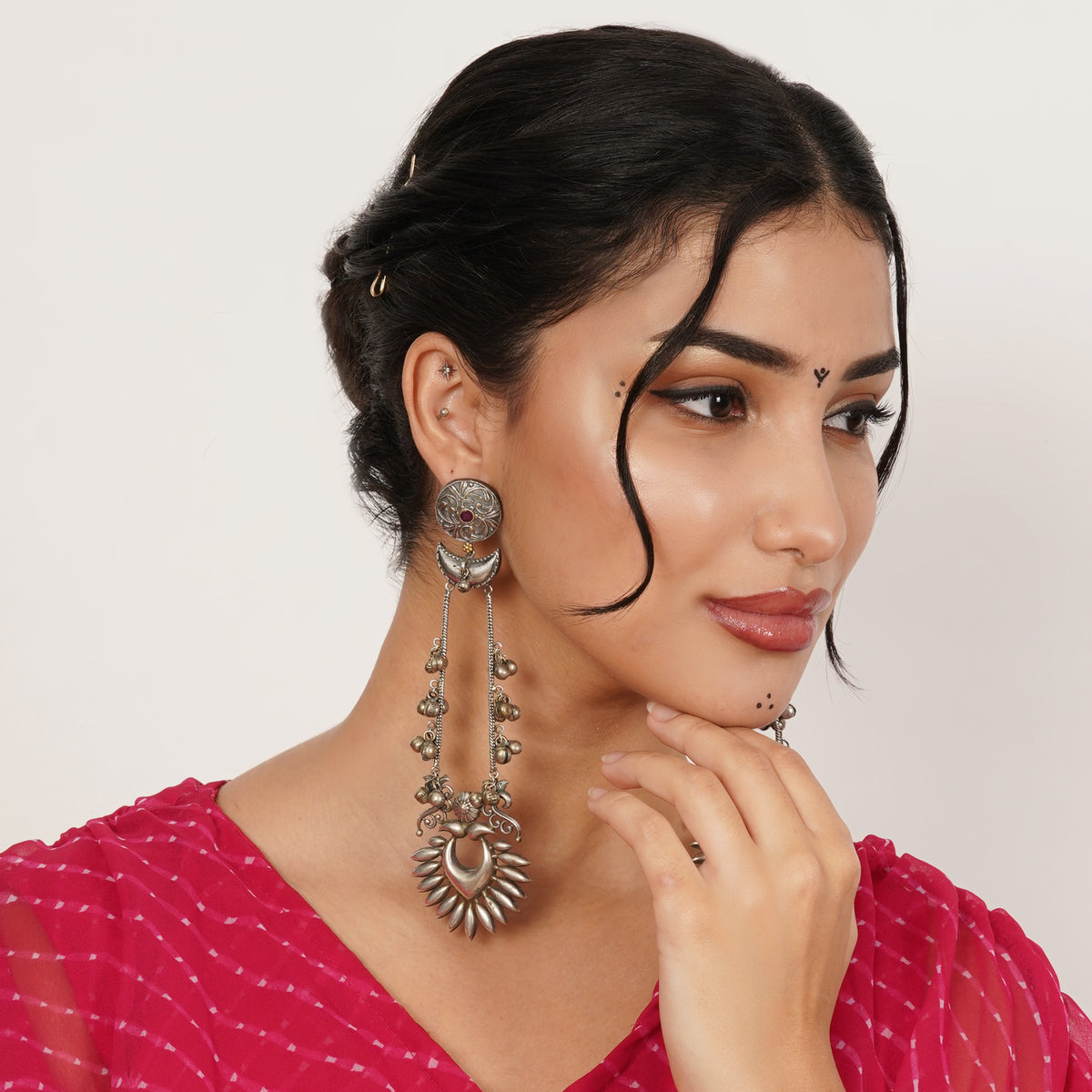 A woman wearing a pair of large, ornate silver-toned dangle earrings with intricate filigree and beadwork