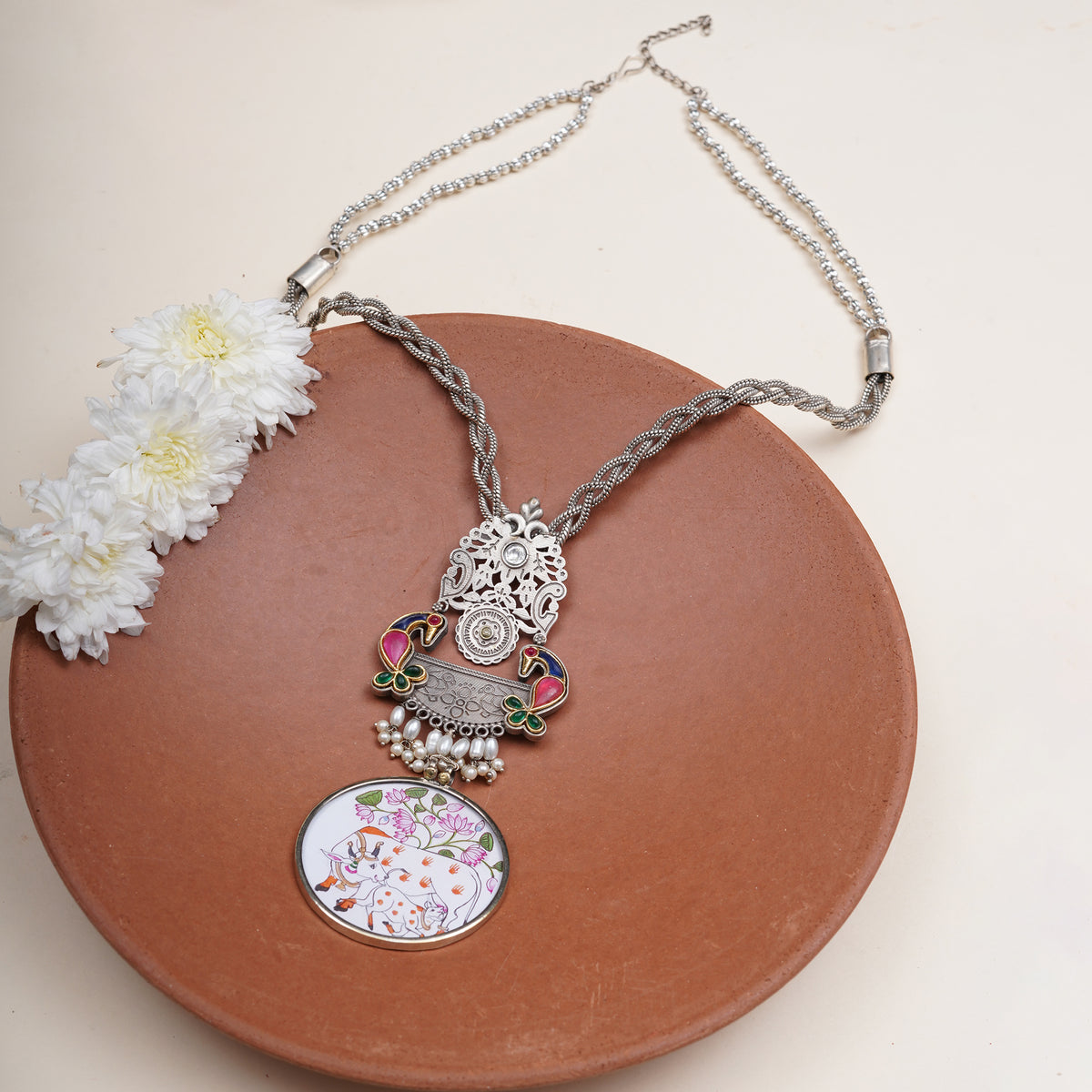 A silver-toned necklace with a detailed pendant featuring a silver elephant, colorful enamel accents, and a round floral pendant