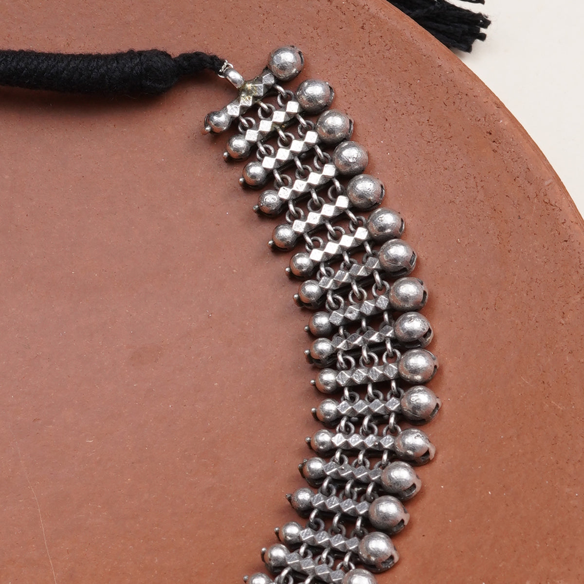 A close-up of a silver-toned beaded necklace with a black tassel