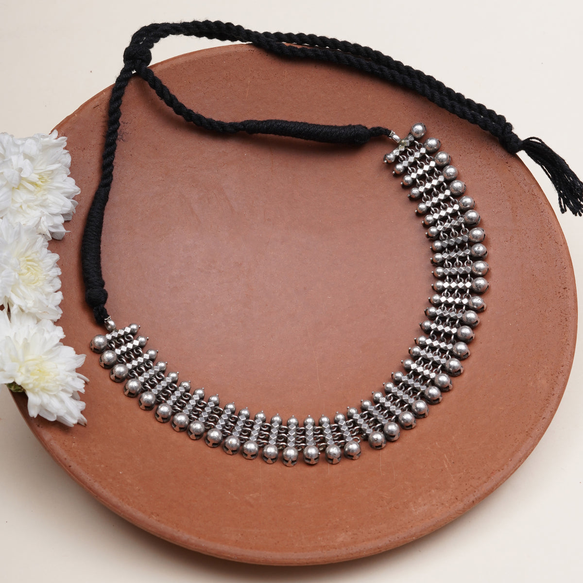 A silver-toned beaded collar necklace with a black braided cord and tassel.