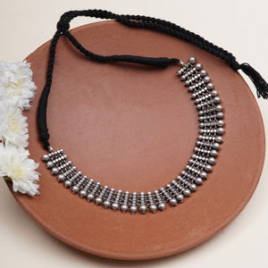 A silver-toned beaded collar necklace with a black braided cord and tassel.