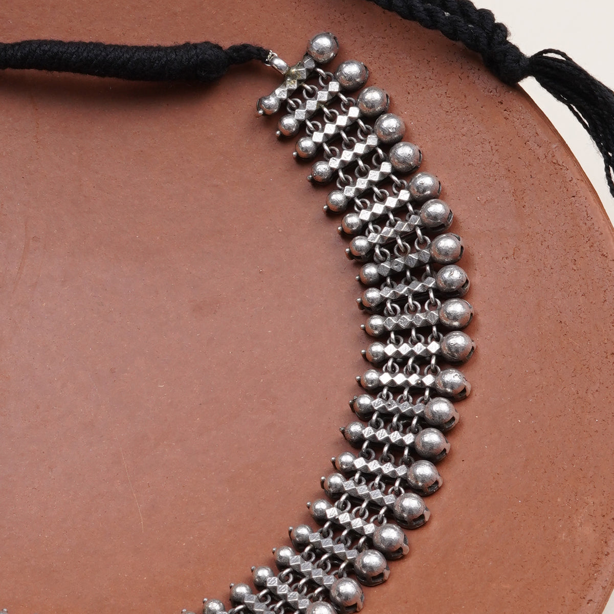 A close-up of a silver beaded choker necklace with a black cord
