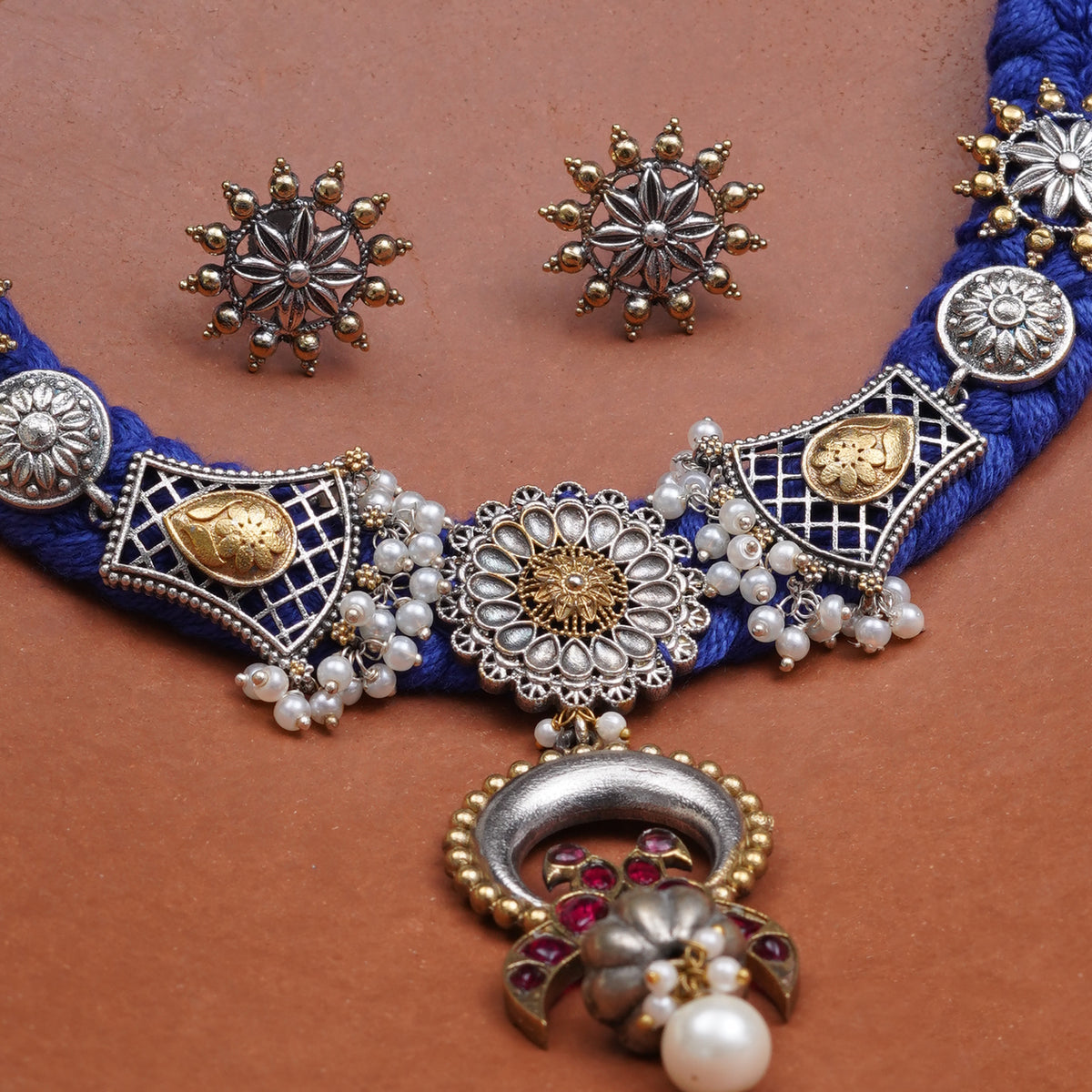 A traditional Indian jewelry set featuring a royal blue and silver-toned necklace with a large central pendant, matching star-shaped stud earrings, and pearl accents