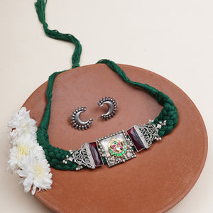 A green braided necklace with ornate silver-toned metal accents and a central decorative panel
