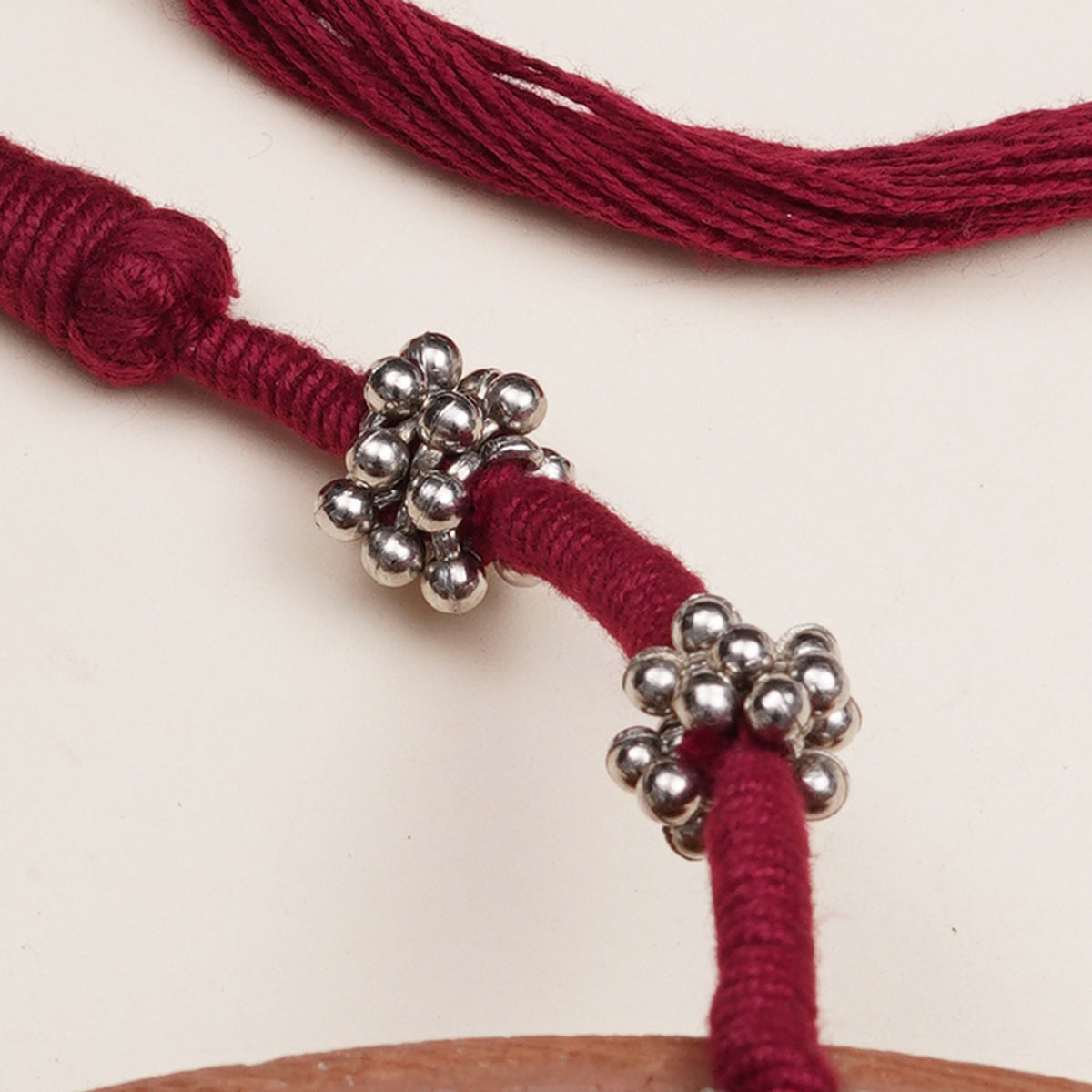 A close-up of a dark red braided cord  necklace with two silver metallic bead clusters