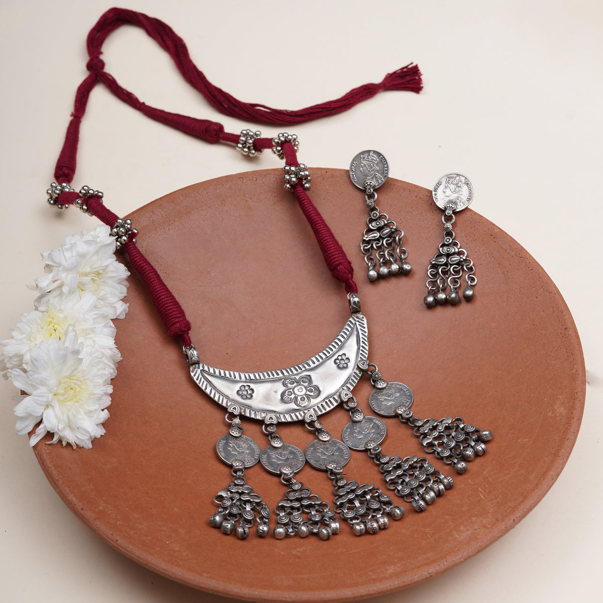 A traditional Indian silver necklace and matching earrings with red cord.