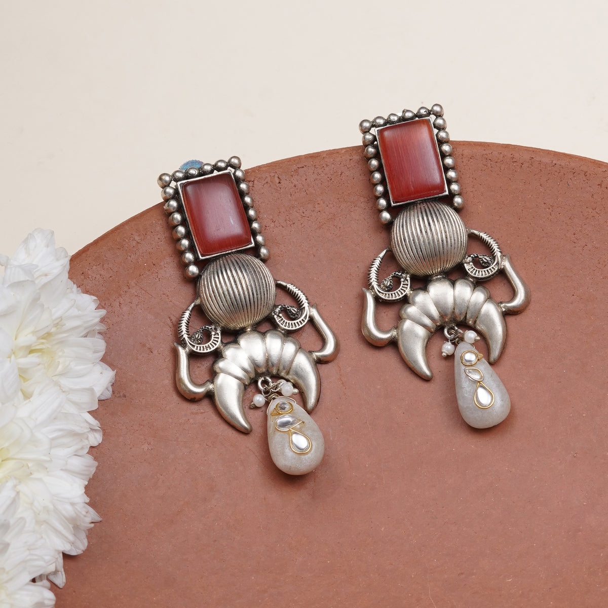 A pair of silver-toned Tibetan-style dangle earrings with rectangular red cabochon stones, textured silver beads, curved silver elements, and teardrop-shaped white stones
