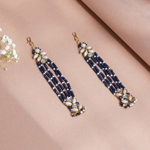 A pair of long gold-tone dangle earrings with white and navy beaded tassels.