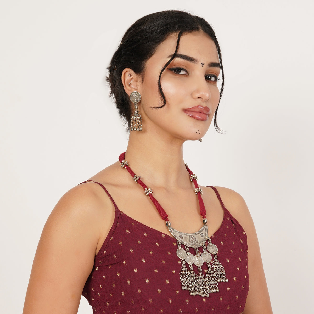 A woman wearing a deep red beaded necklace with a silver-toned ornate pendant and matching dangling earrings